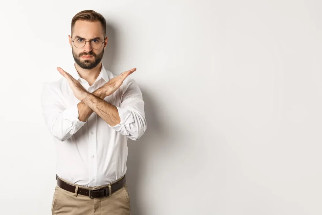 Homem com expressão séria, braços cruzados em forma de X, representando rejeição ou recusa.