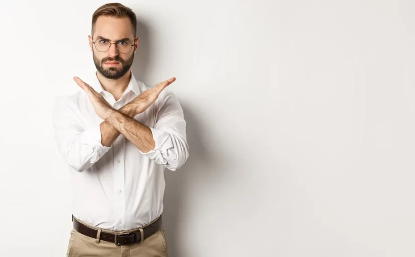 Homem com expressão séria, braços cruzados em forma de X, representando rejeição ou recusa.