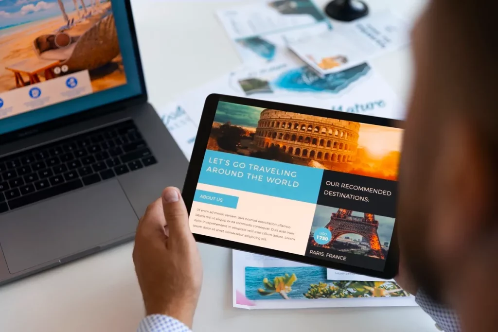 Pessoa segurando tablet com landing page de turismo exibindo destinos famosos, como o Coliseu em Roma e a Torre Eiffel em Paris, ao lado de um notebook com imagem de praia