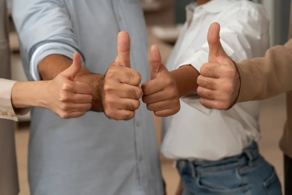 Mãos de pessoas de uma equipe fazendo sinal de positivo com os polegares levantados, representando feedback positivo e união