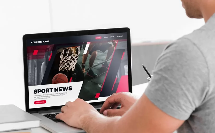 Pessoa acessando uma página de notícias esportivas em laptop com imagens de basquete e design moderno em vermelho e preto