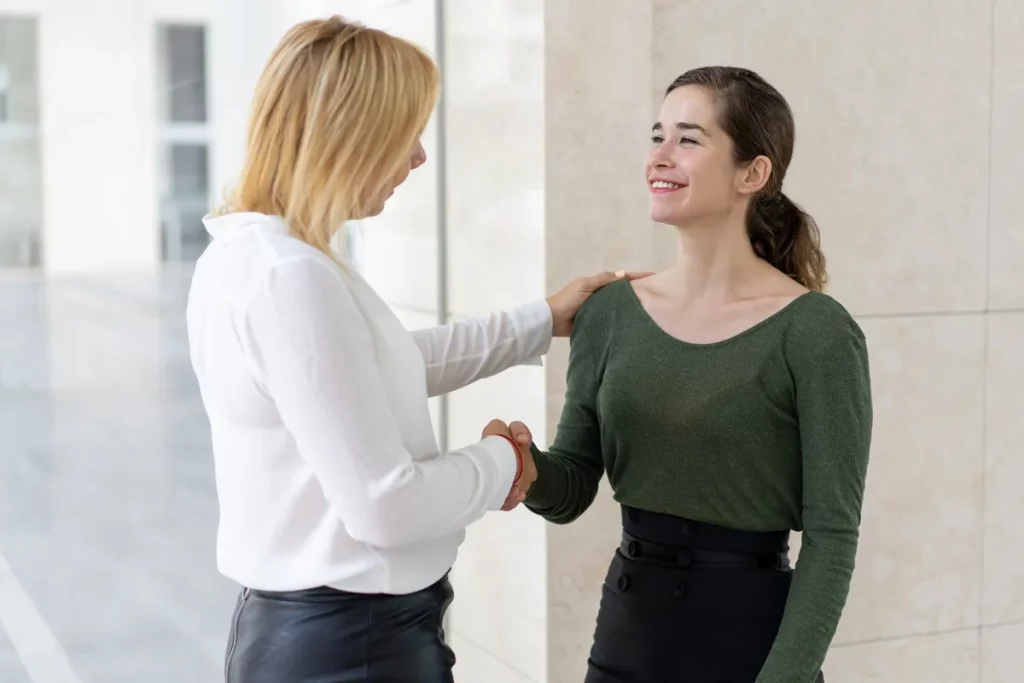 Duas mulheres em um ambiente corporativo, trocando um aperto de mão amigável e expressando linguagem corporal positiva.