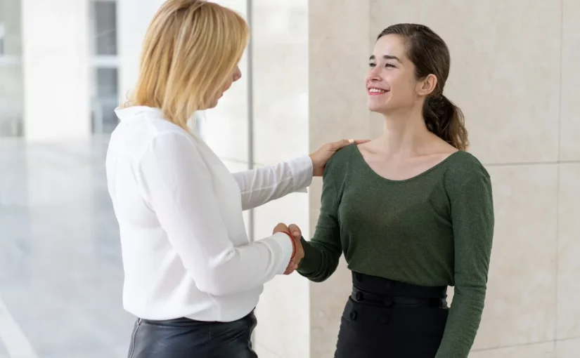 Duas mulheres em um ambiente corporativo, trocando um aperto de mão amigável e expressando linguagem corporal positiva.