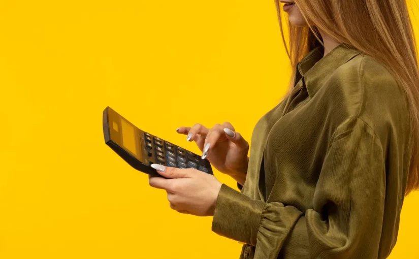 Mulher com camisa verde usando uma calculadora sobre fundo amarelo, simbolizando controle financeiro e análise de despesas