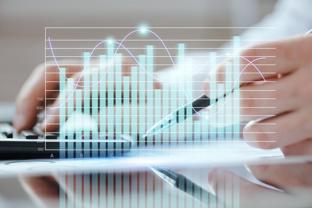 Mãos segurando uma caneta e digitando em uma calculadora, com um gráfico digital sobreposto representando análise de dados financeiros.